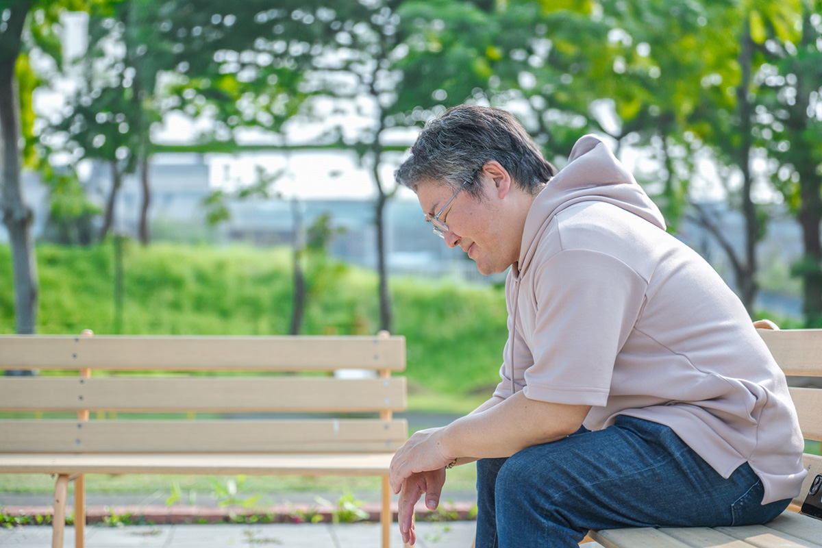 伸び放題の庭木や植木屋への依頼について悩み、公園のベンチでうつむいてため息をついている男性のイメージ
